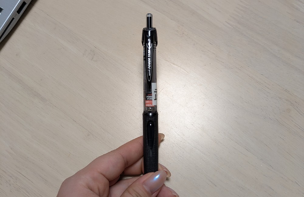 指先で持った三菱鉛筆の加圧式ボールペン「パワータンク」。屋外や速記が必要な現場でも確実に筆記できる、行政書士の業務を支えるプロ仕様の文房具。